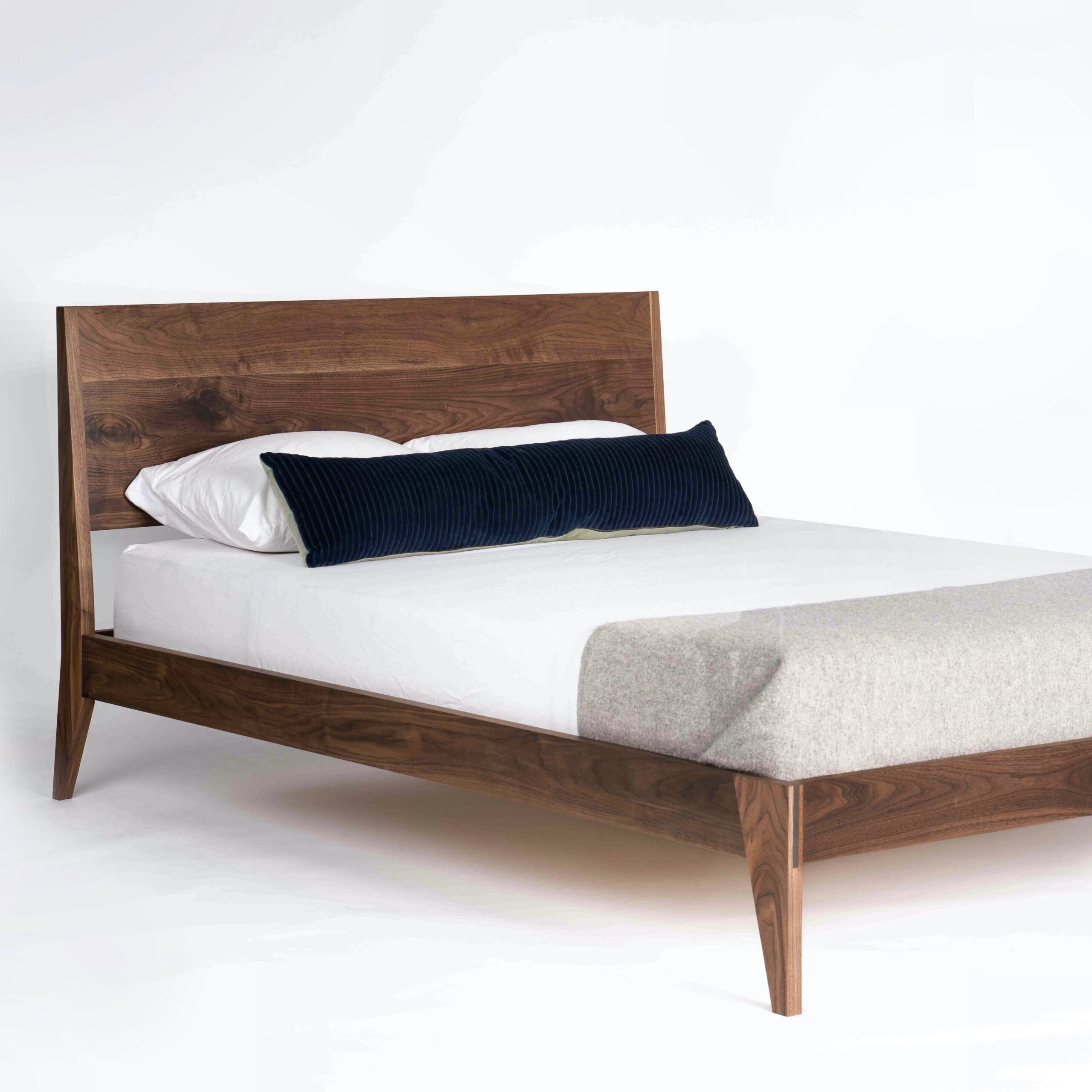 A simple all solid walnut bed with a mattress and pillows on it. Mortise and tenon joinery used at the footboard.