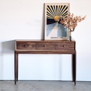 A walnut entry table with turned legs and three drawers in a row with small brass pulls.