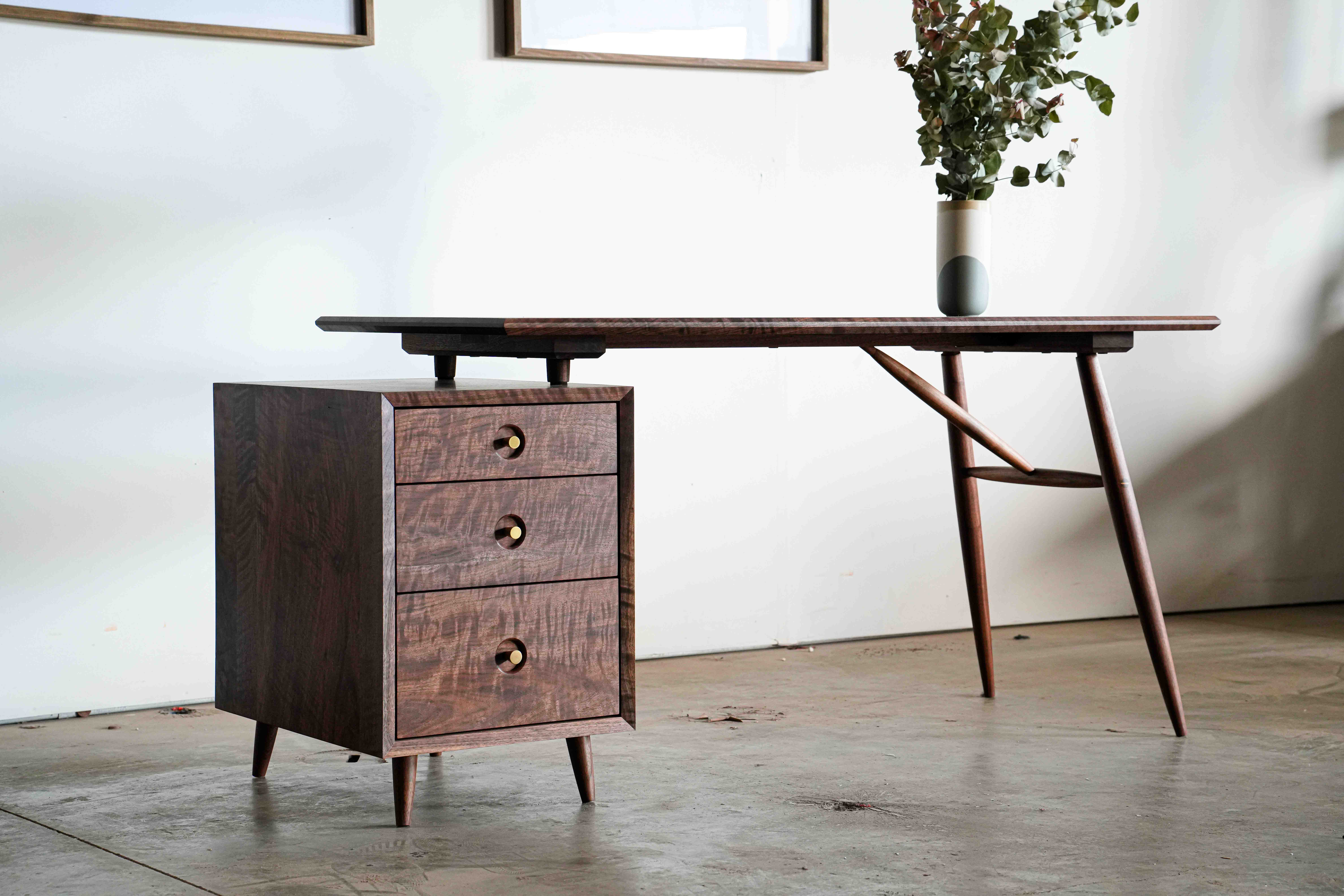 A walnut desk with a box of three drawers on the left and simple turned legs on the right. All walnut, called the Muir Writing Desk.