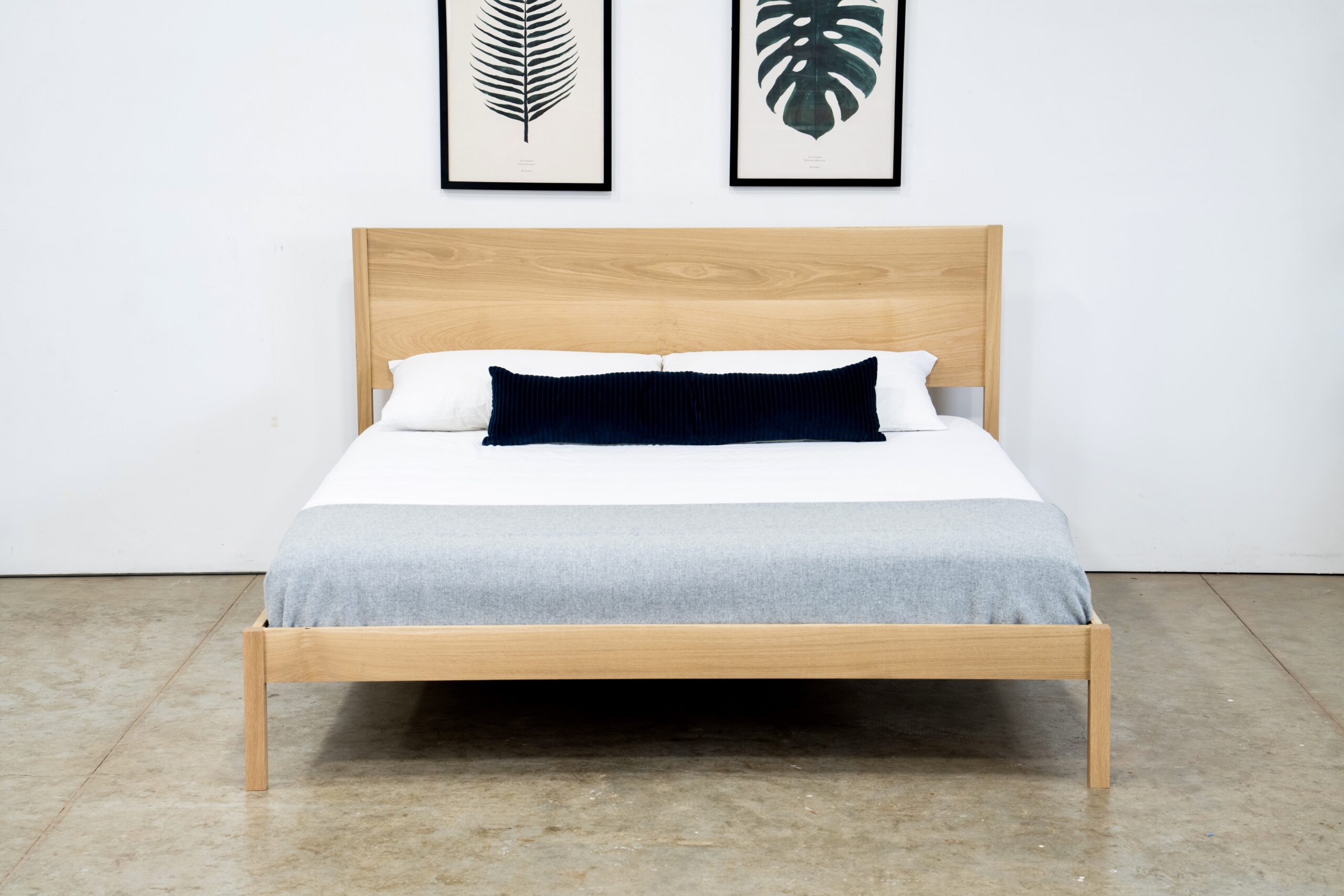 A simple platform bed in white oak with a mattress and pillows.