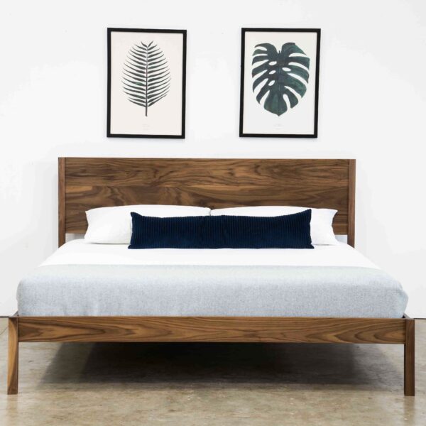 A simple bed made of solid walnut. Has a mattress and pillows.