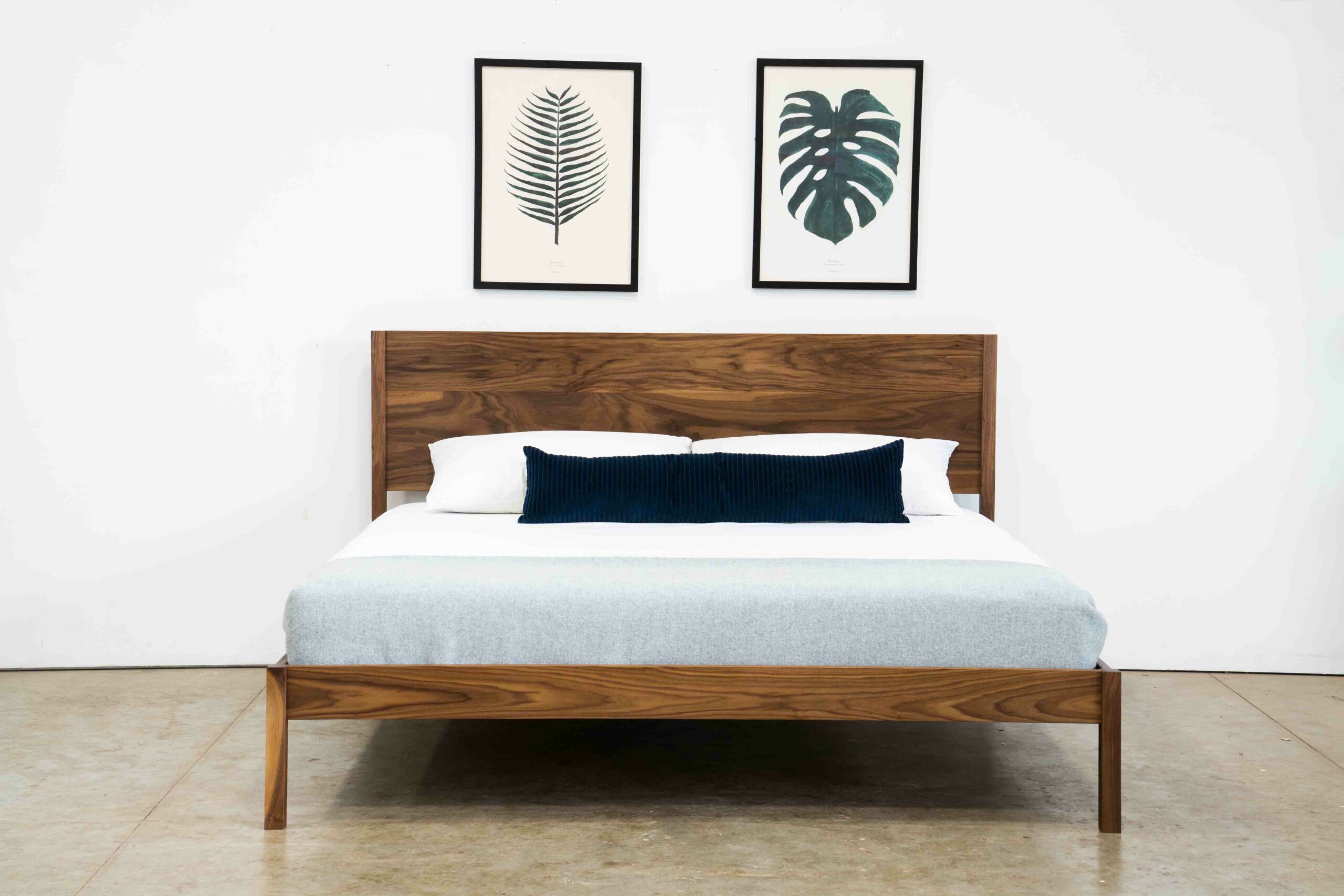 A simple platform bed made of walnut with a mattress and pillows.