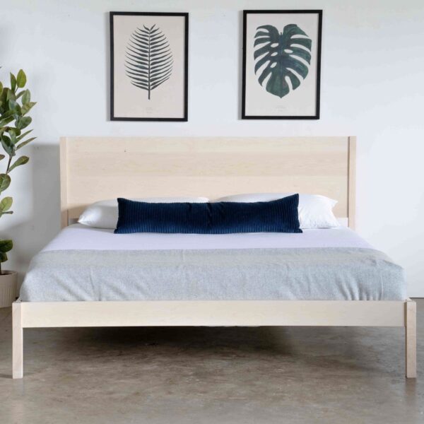 A simple maple bed with a mattress and pillows.
