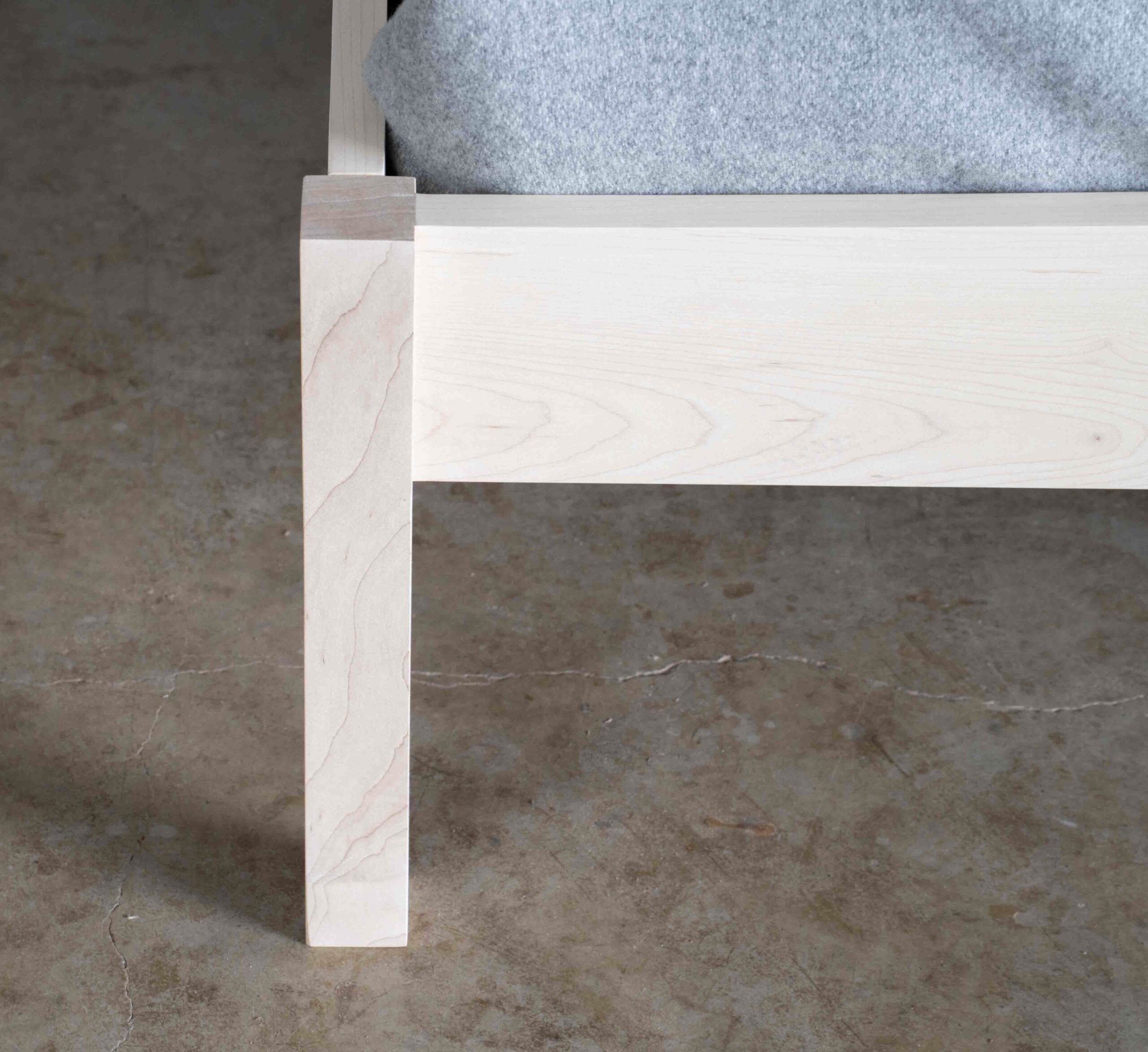 A closeup of the foot of a simple platform bed made of maple.