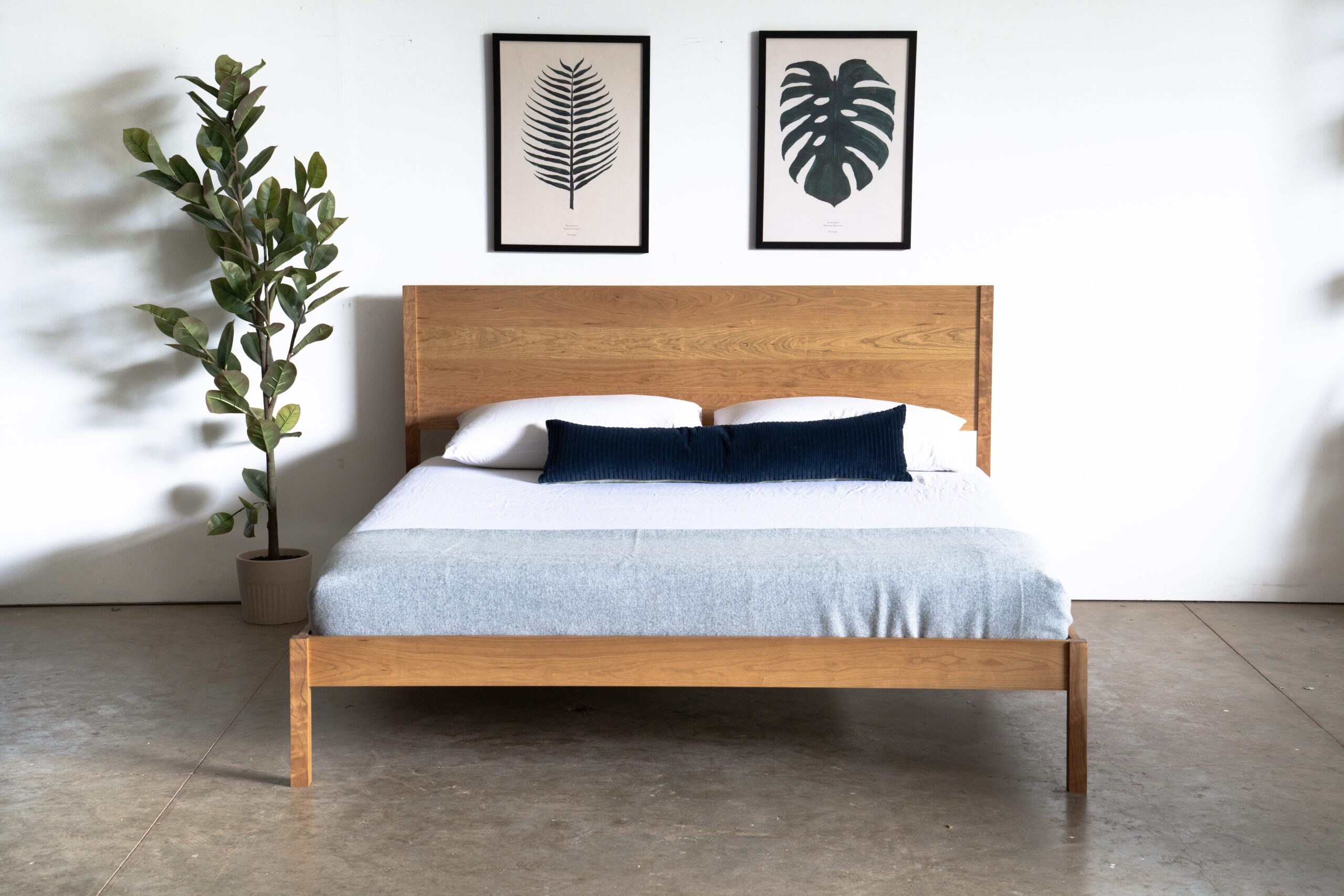 A simple solid cherry bed with a mattress and pillows next to a plant.