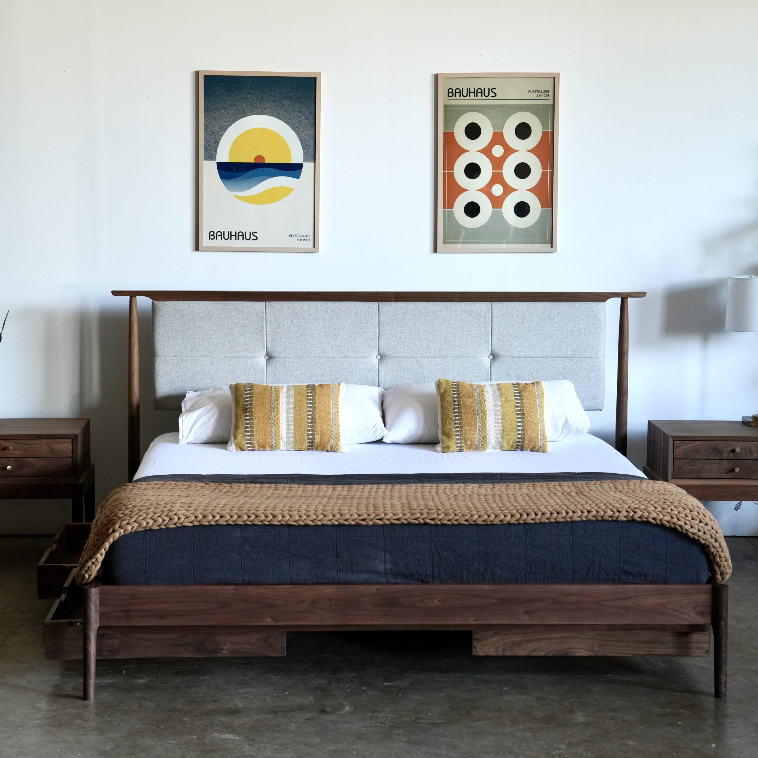 A walnut midcentury modern bed with an upholstered headboard that appears to float and drawers suspended from beneath. The headboard is an oatmeal color.