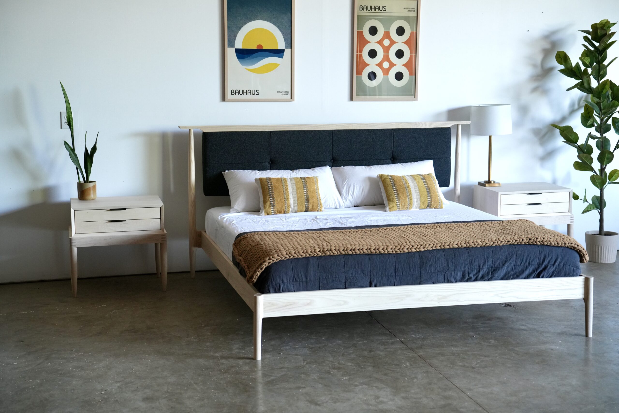 A maple midcentury modern bed with an upholstered headboard that appears to float and drawers suspended from beneath. The headboard is a charcoal color.
