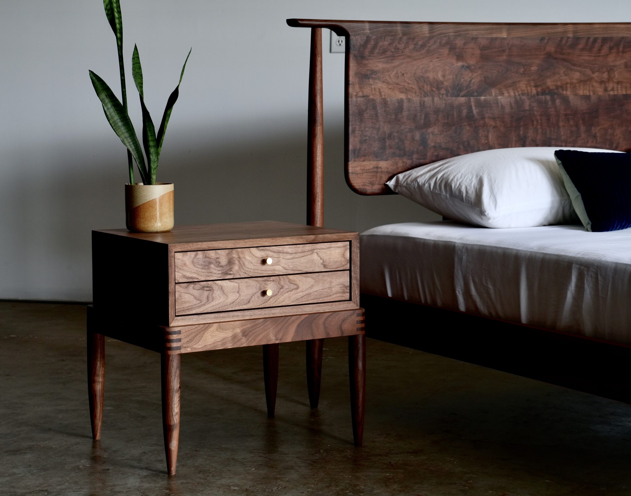 A midcentury modern bed with a figured walnut headboard next to a matching nightstand