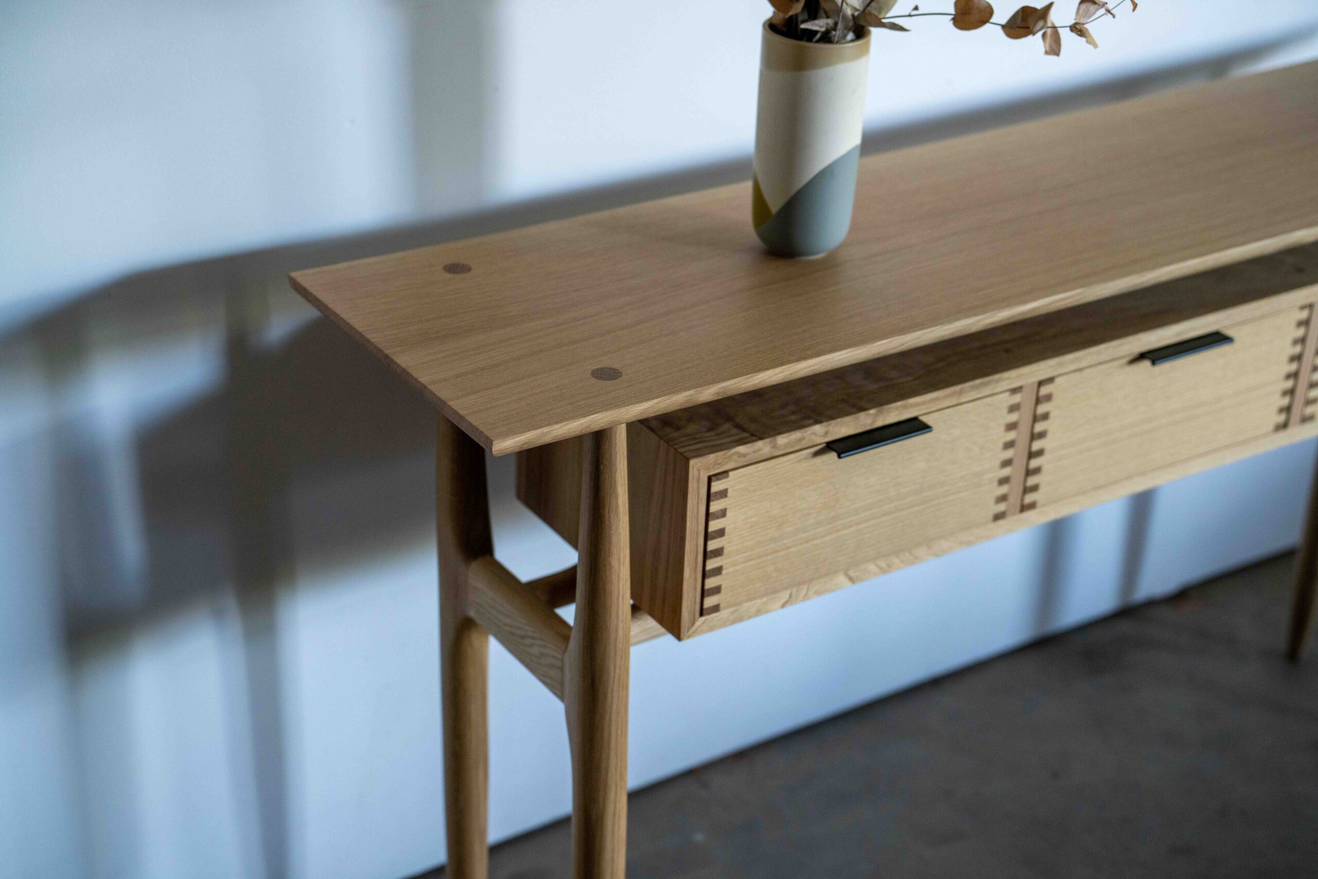 A midcentury modern entry table in white oak with black drawer pulls