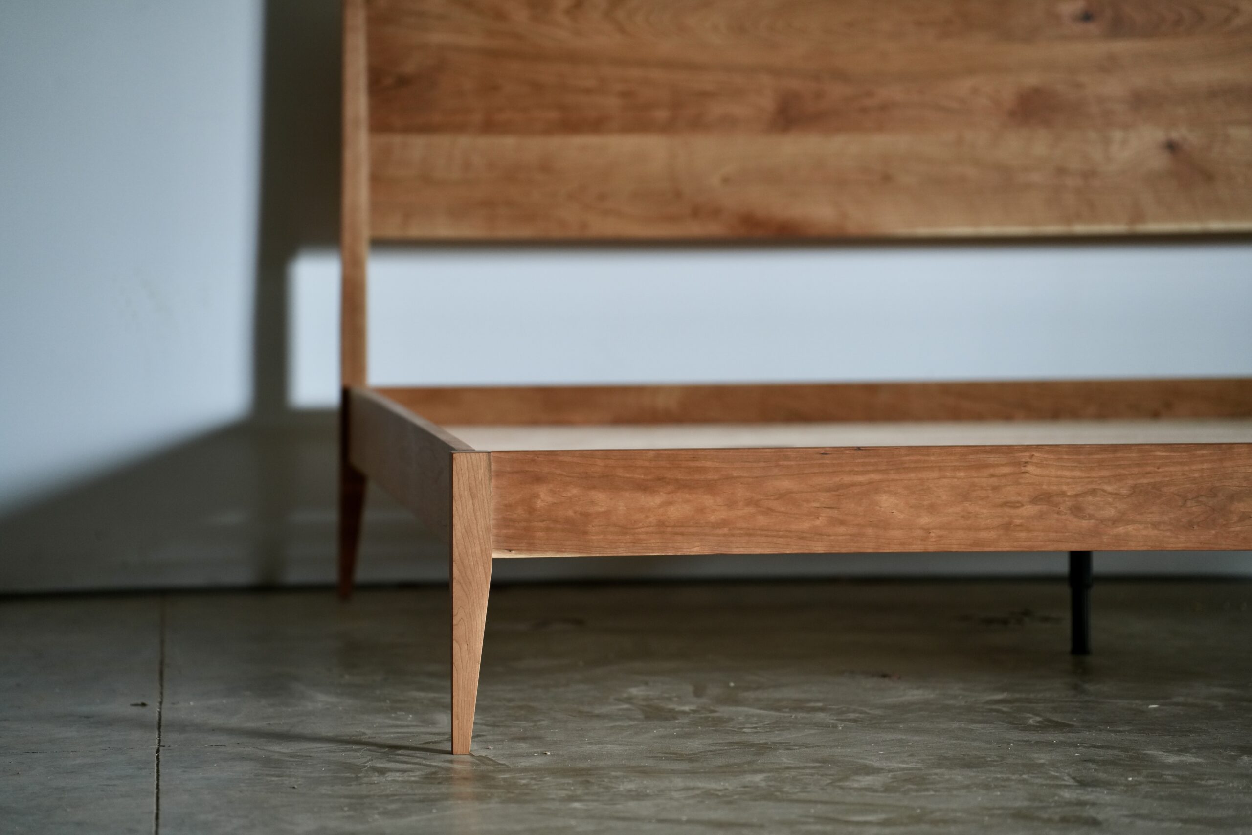 A close-up of the tapered leg on a cherry shaker style bed.