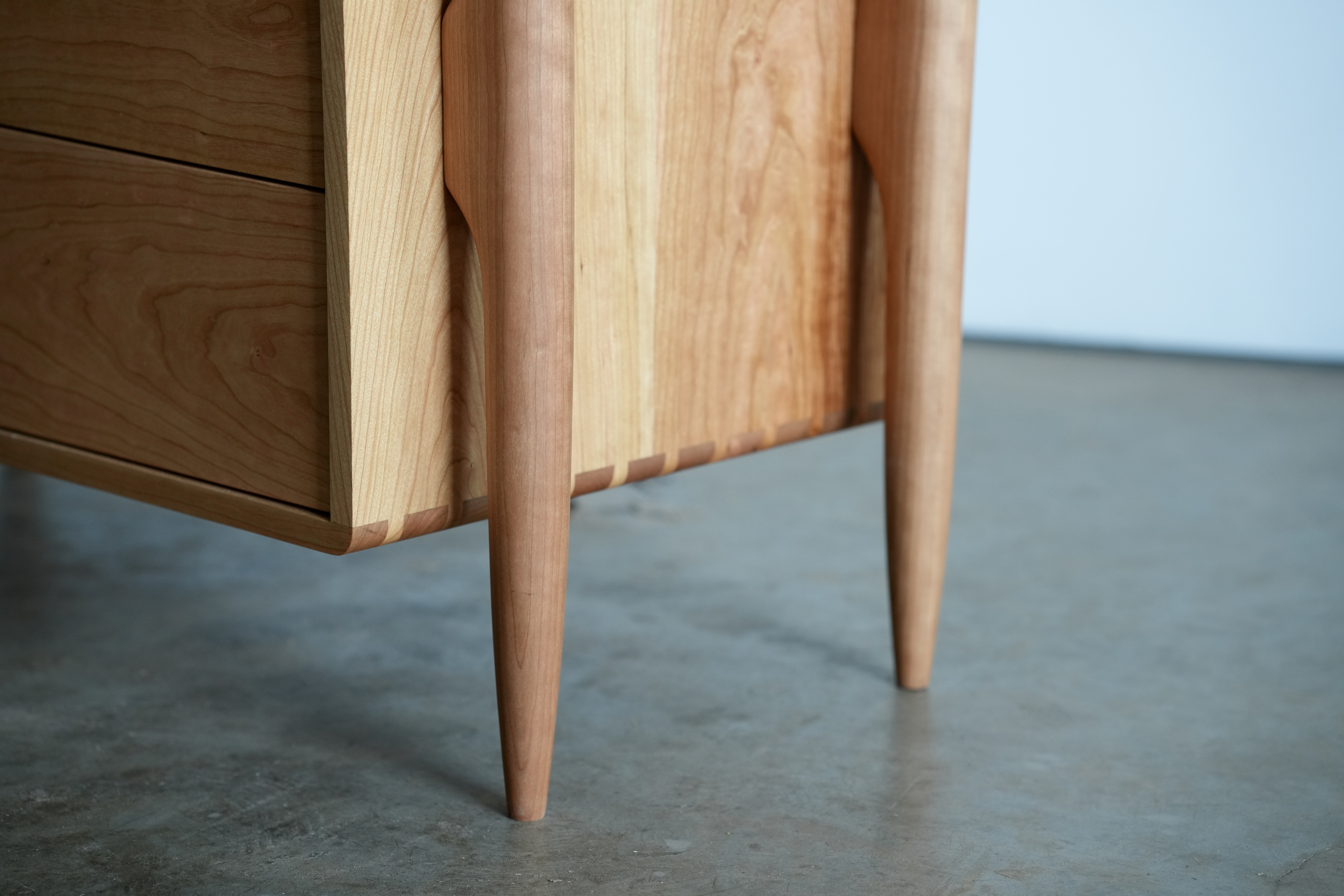 A close-up of the legs of a cherry midcentury modern dresser