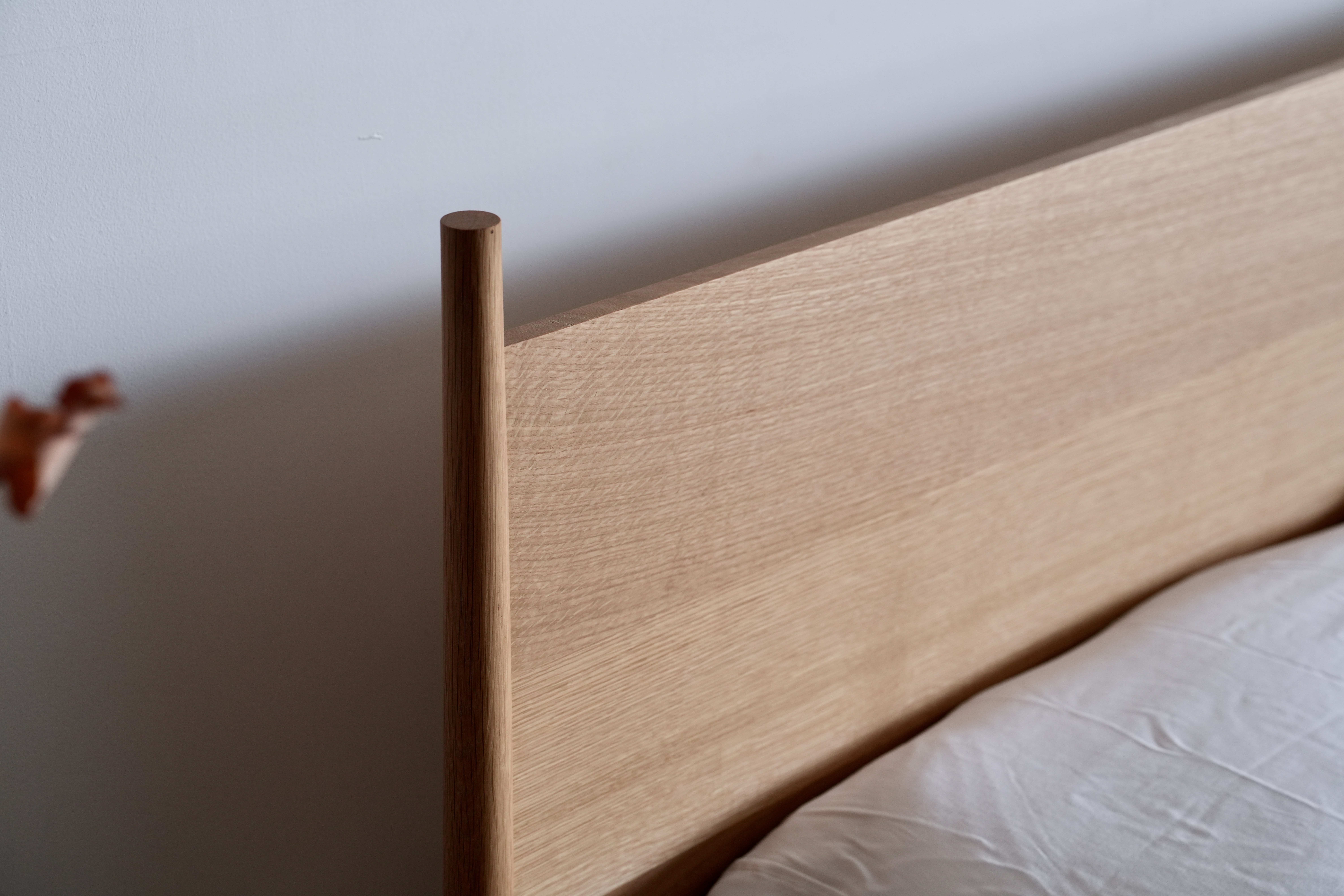 Close-up of a white oak headboard with a turned upright post that extends above the headboard.