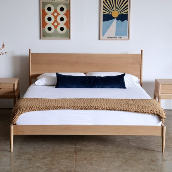 A simple midcentury modern bed in white oak with a blue pillow and yellow throw blanket at the foot.