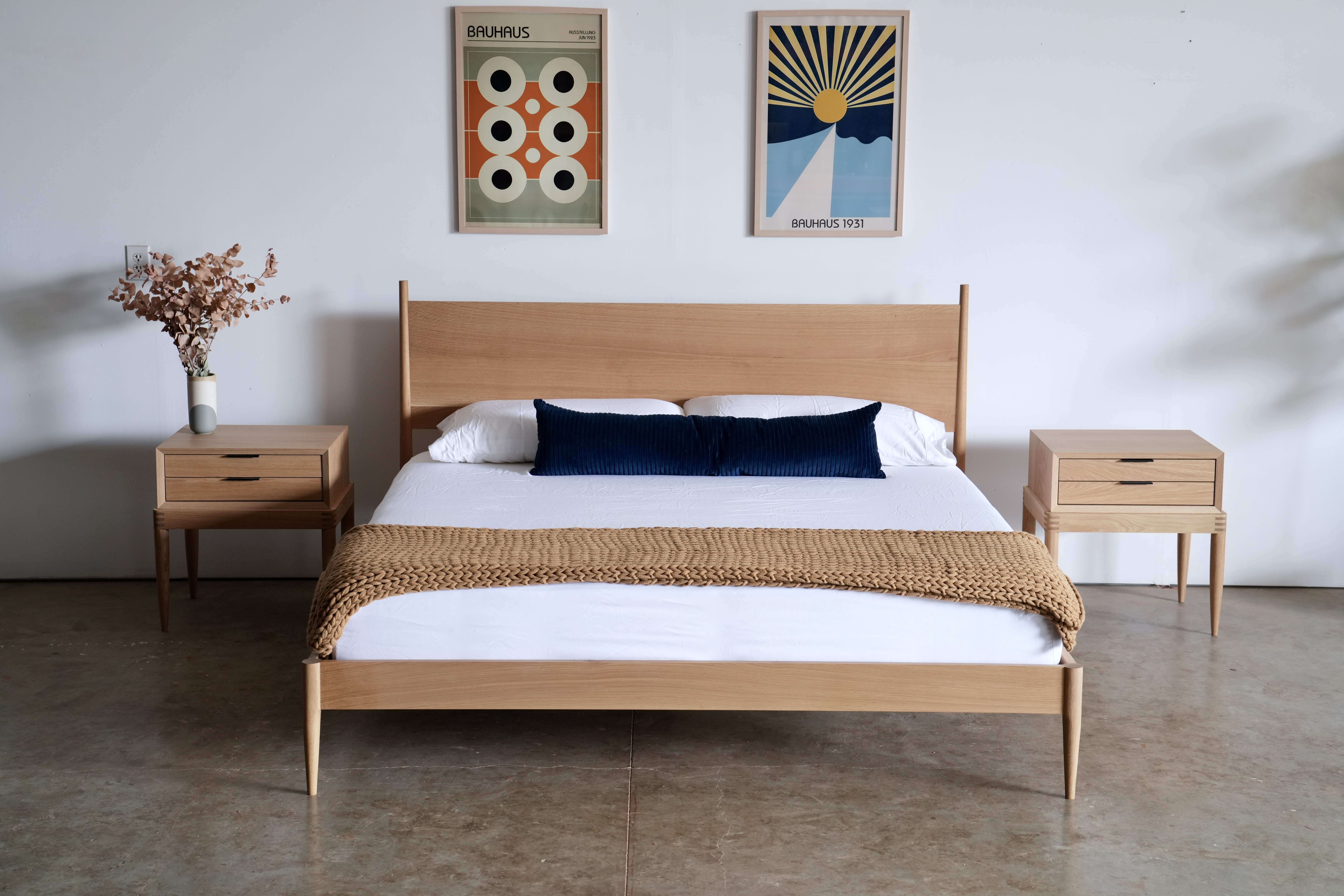 A simple midcentury modern bed in white oak with a blue pillow and yellow throw blanket at the foot.