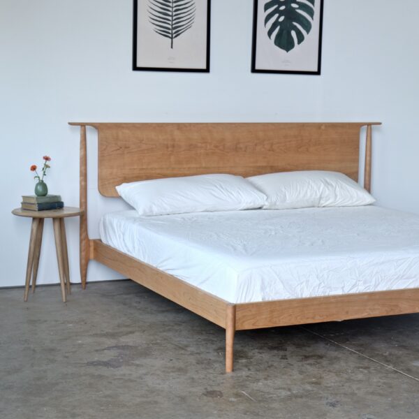 A solid cherry midcentury modern style bed with a headboard that appears to float. Next to it is a simple round tabletop nightstand.