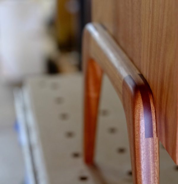 A close-up of the rounded leg of a mahogany nightstand