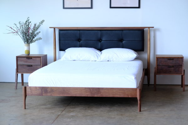 A walnut midcentury modern bed with an upholstered headboard that appears to float. The headboard is black leather.