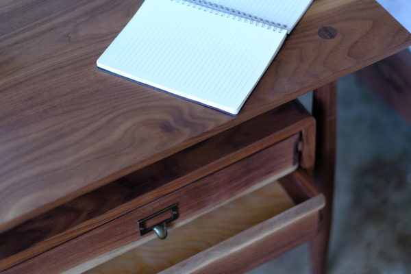 A closeup of the drawers of a handmade side table that is Scandinavian style, with the drawers appearing to float under the table top and made of solid walnut.