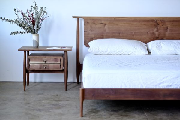 A midcentury modern bed and nightstand, both made from walnut.