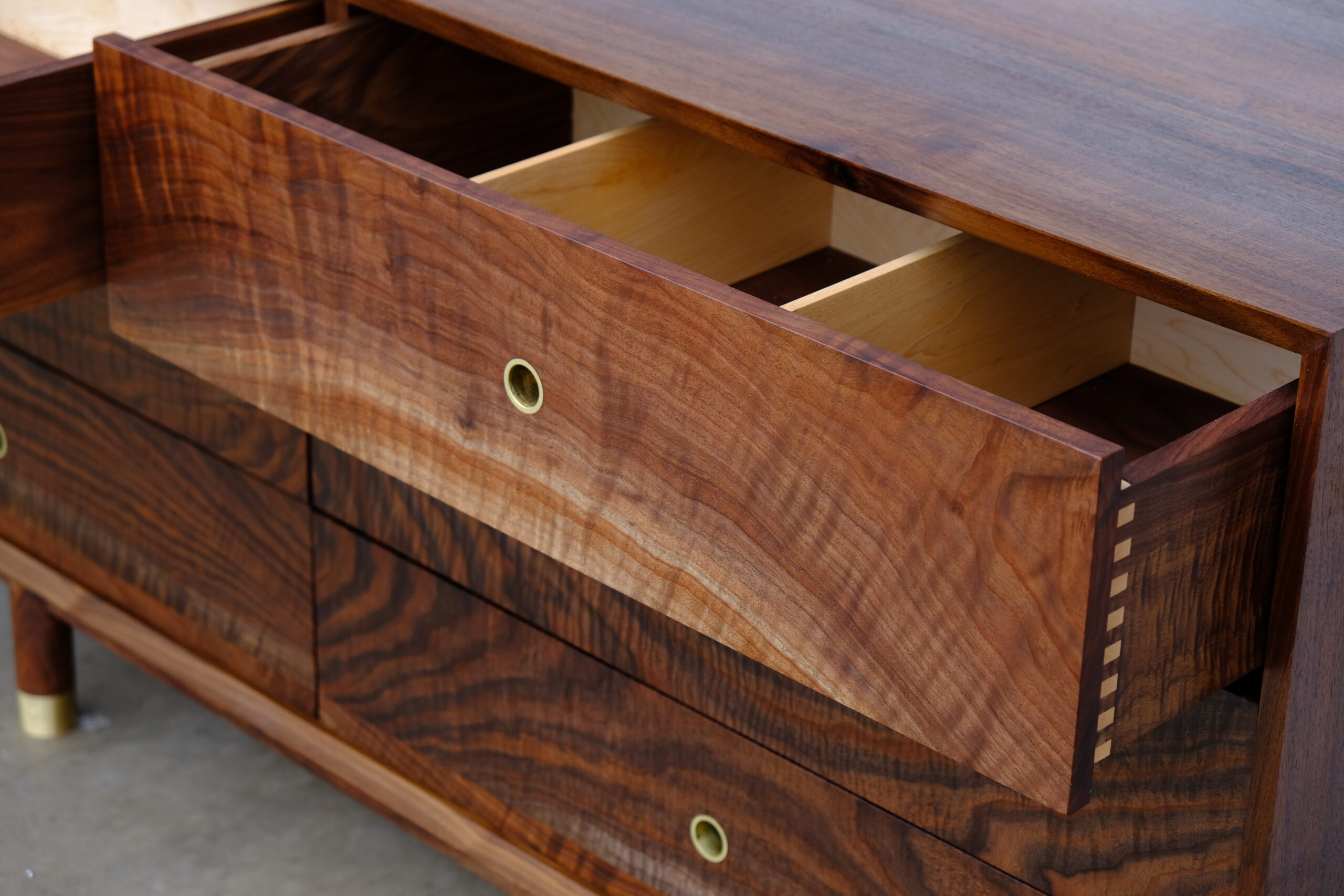 Close up of an open drawer with dividers and an inlaid brass pull.