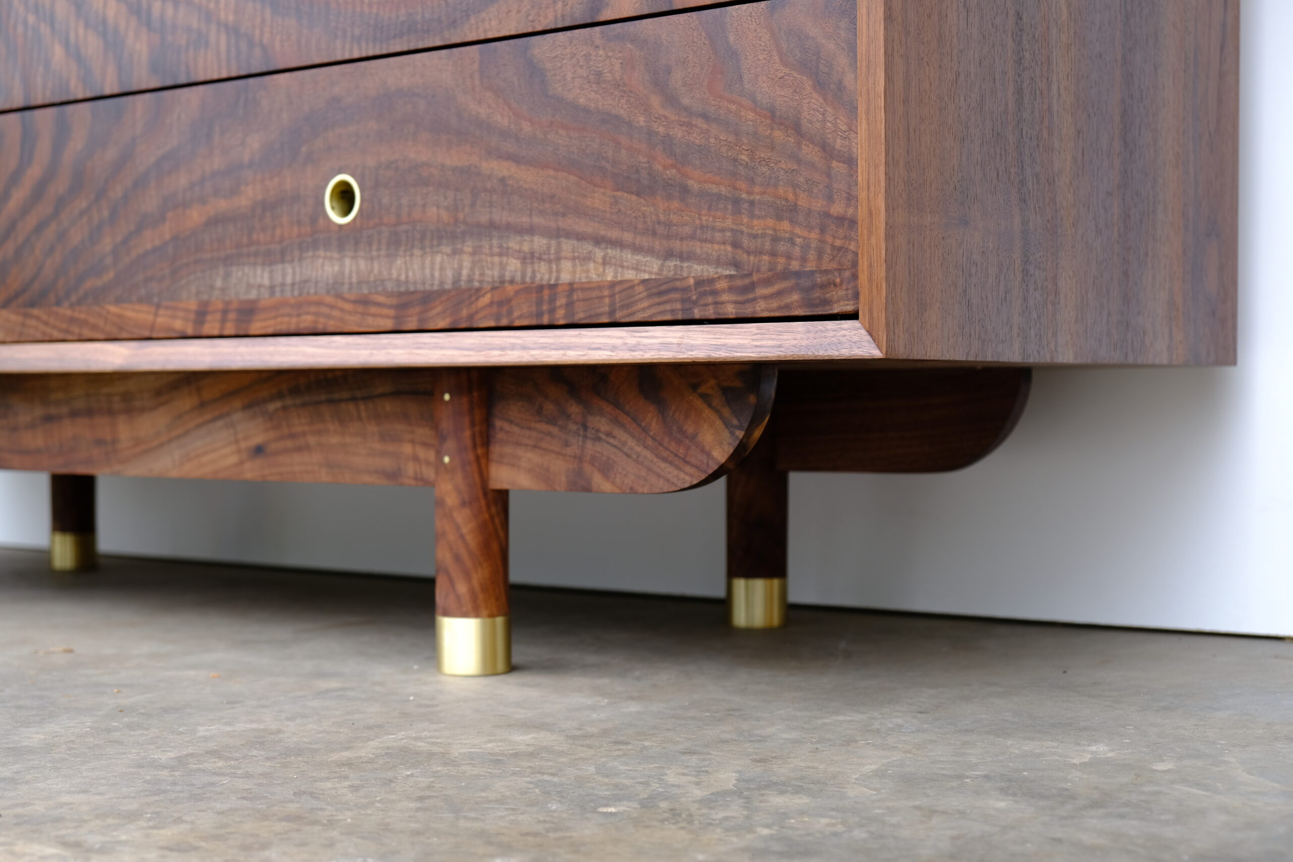 Close up of feet of walnut dresser that have brass caps on the bottom.