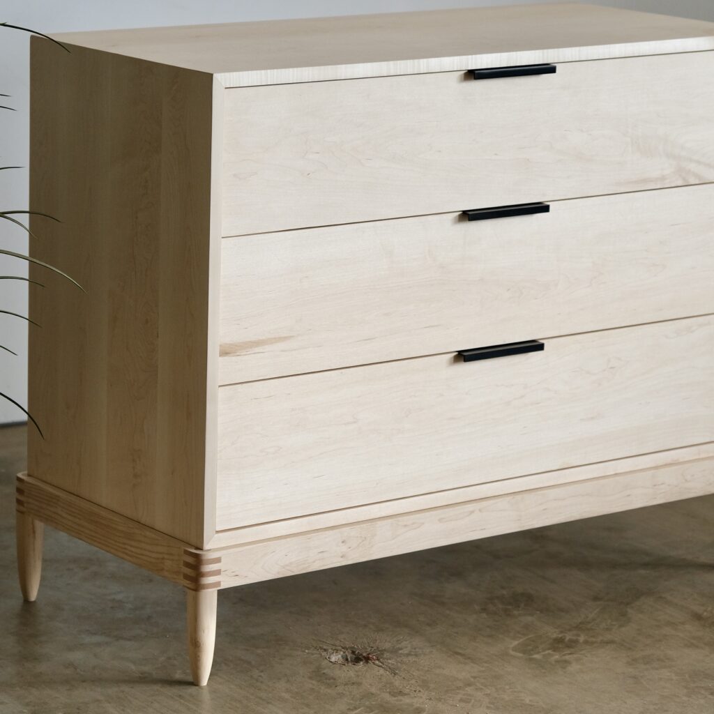 A maple dresser with three drawers and black handles
