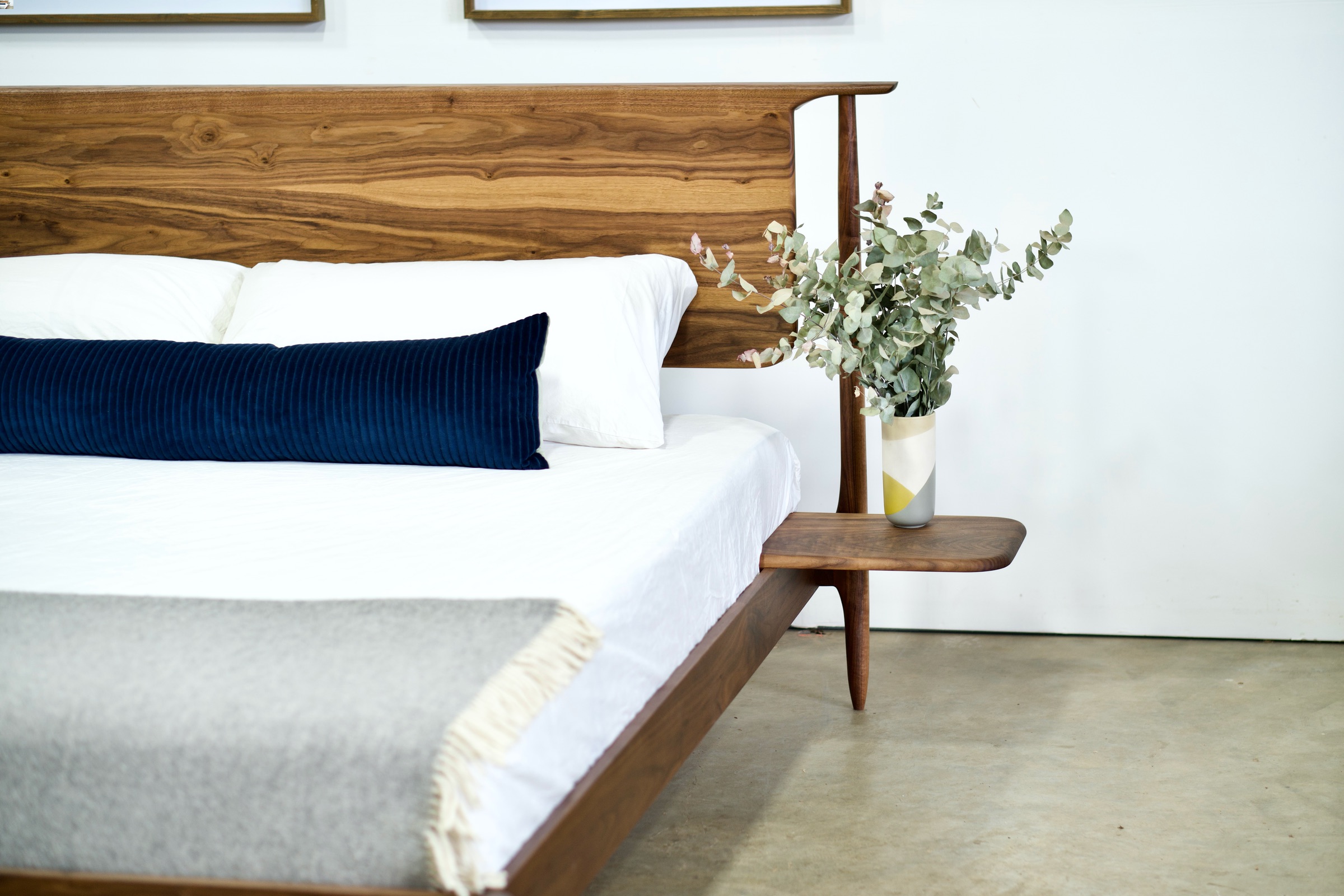 A walnut bed with a headboard that appears to float and a simple side table/shelf attached to the side of the bed