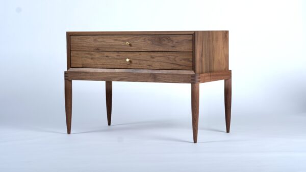 A simple two-drawer walnut nightstand with exposed joiner at the base and conical brass pulls.