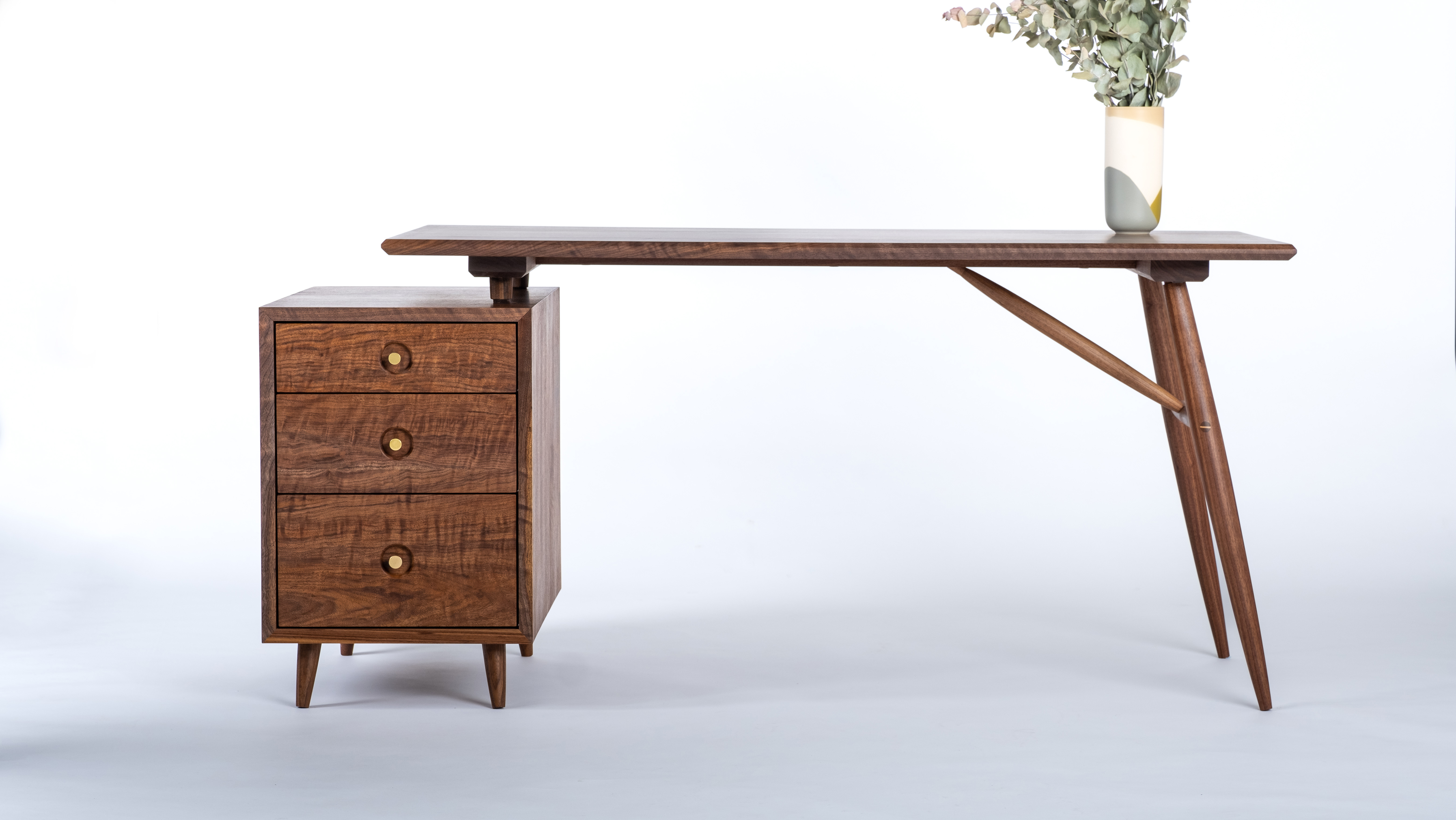 A walnut desk with a box of three drawers on the left and simple turned legs on the right. All walnut, called the Muir Writing Desk.