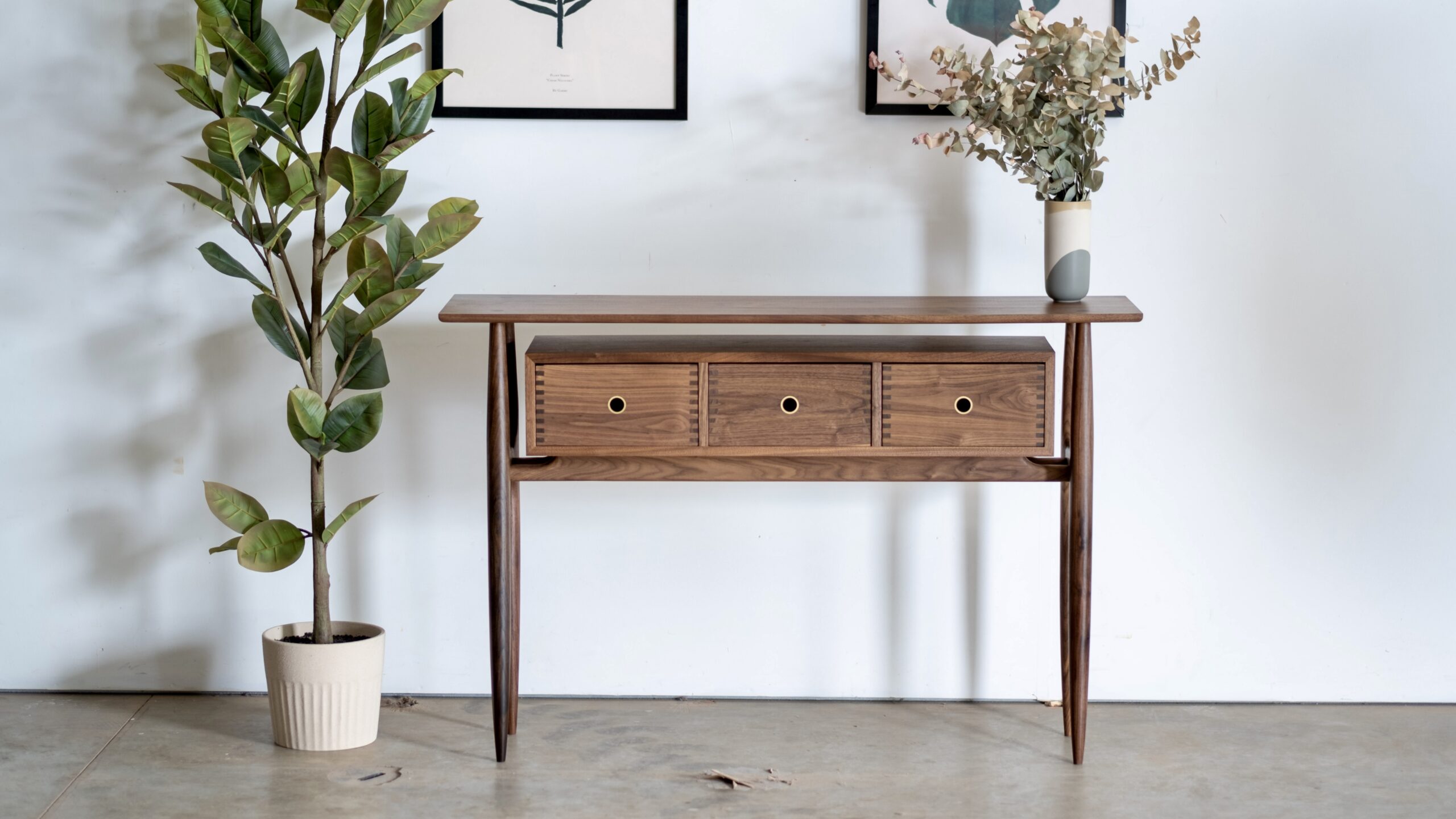 A walnut entry table with round tapered legs and a box with three drawers suspended in a way it appears to float. The pulls are circular cutouts with inlaid brass.
