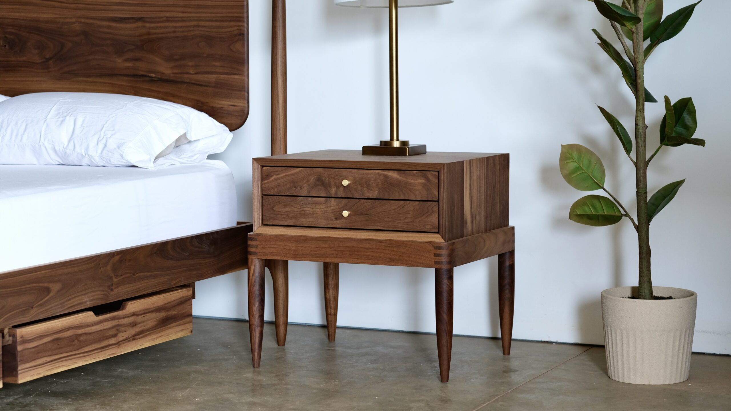 A solid wood nightstand made of walnut with two shallow drawers and round brass pulls.