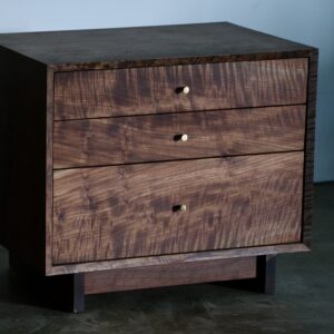 A solid wood side table made of walnut with three drawers and conical brass knobs.