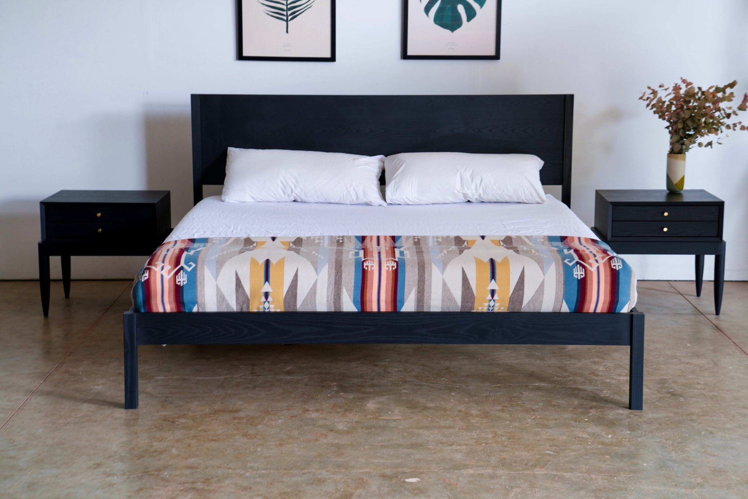 A simple platform bed made of ebonite ash, with a mattress and pillows and nightstands.