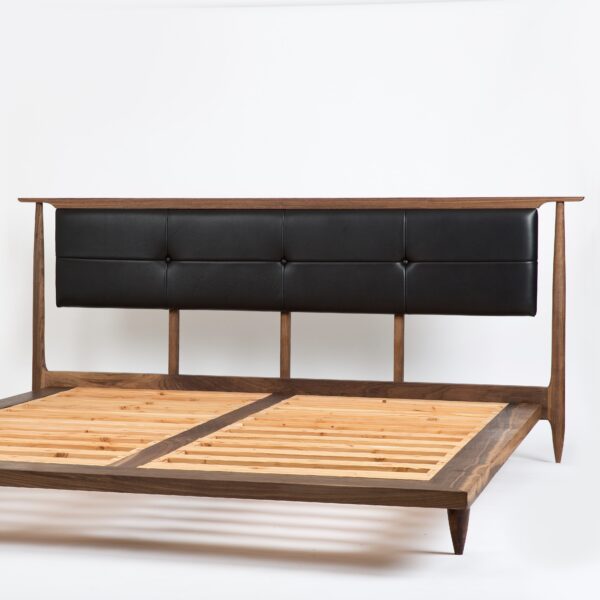 A solid walnut platform bed with an upholstered black leather headboard.