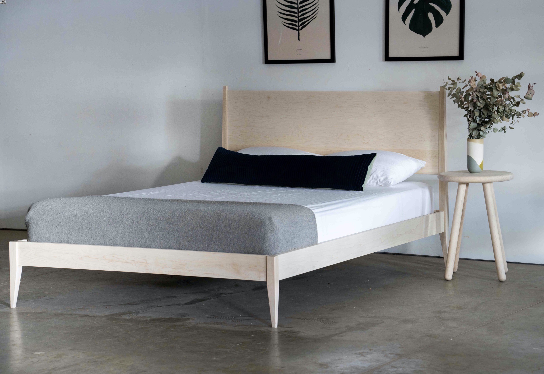 A maple shaker style midcentury modern bed with tapered legs. A mattress, pillows, and a gray blanket are on the bed.
