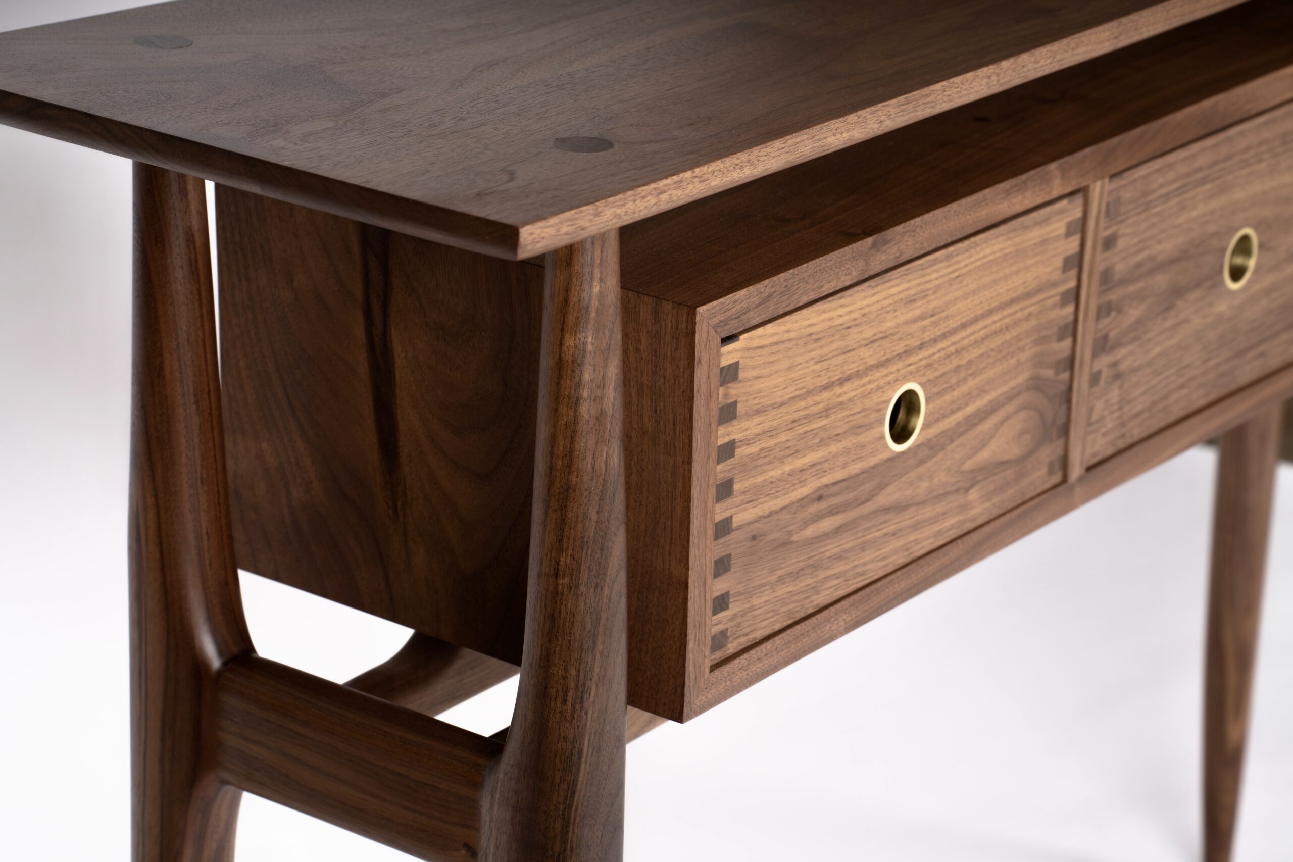 A walnut entry table with round tapered legs and a box with three drawers suspended in a way it appears to float. The pulls are circular cutouts with inlaid brass.